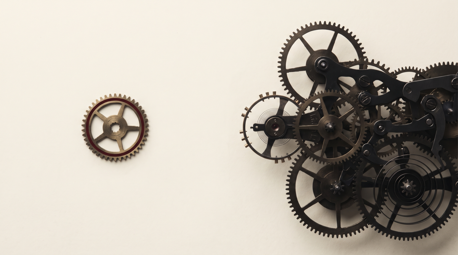 A single small brass gear set apart on the left, facing a dense cluster of interlocking dark clockwork gears on the right, on a cream background.
